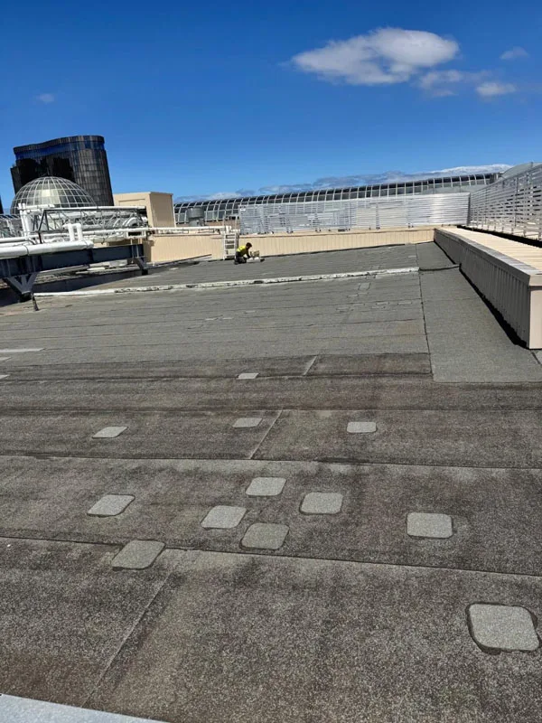 Roofing crew installing torch on membrane waterproofing in Melbourne on flat commercial roof with skylights and equipment curbs