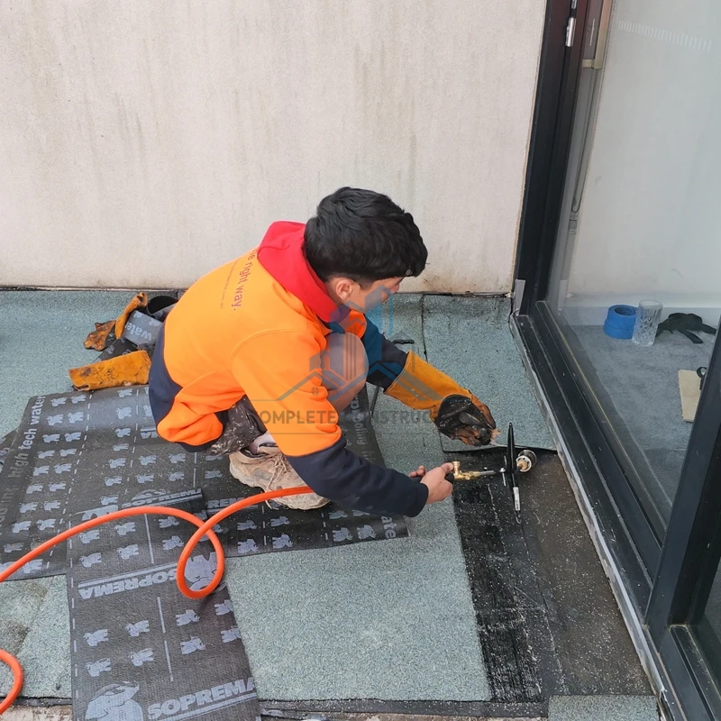 Installing black Soprema waterproofing membrane sheets on a concrete terrace